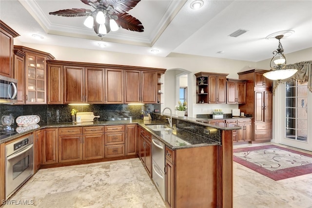 kitchen with appliances with stainless steel finishes, pendant lighting, kitchen peninsula, sink, and a tray ceiling