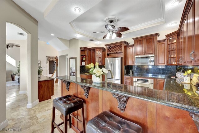 kitchen with appliances with stainless steel finishes, kitchen peninsula, a raised ceiling, and dark stone counters