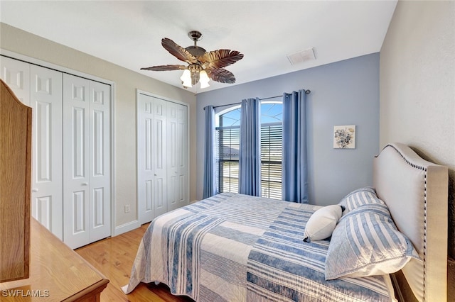 bedroom with hardwood / wood-style flooring, ceiling fan, and two closets