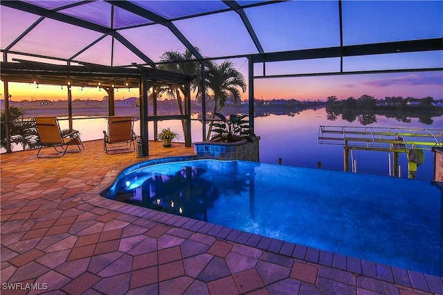 pool at dusk featuring a water view, a patio area, and glass enclosure