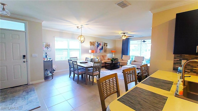 tiled dining area featuring crown molding, sink, and ceiling fan with notable chandelier