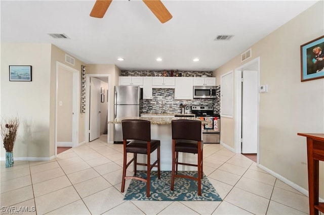 kitchen with appliances with stainless steel finishes, light stone counters, white cabinets, a kitchen bar, and light tile patterned flooring