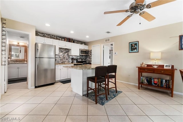 kitchen featuring light tile patterned flooring, white cabinetry, a breakfast bar area, dark stone countertops, and stainless steel appliances