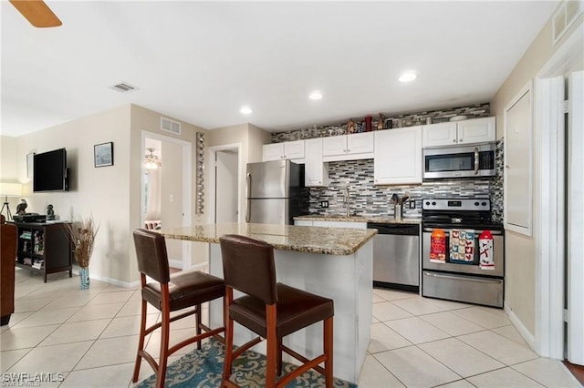 kitchen featuring light tile patterned flooring, a kitchen island, white cabinetry, light stone counters, and stainless steel appliances