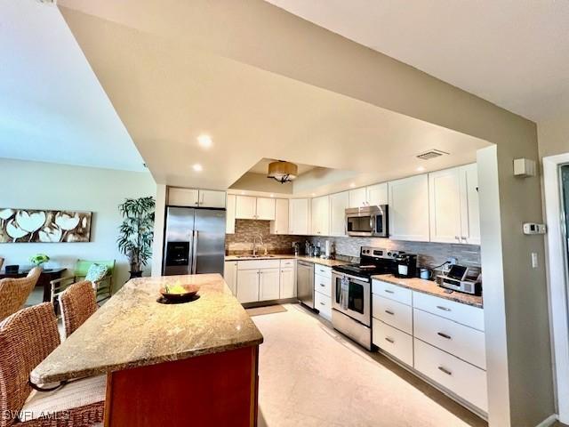 kitchen with a breakfast bar area, appliances with stainless steel finishes, light stone counters, tasteful backsplash, and white cabinets