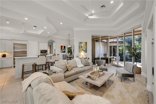 tiled living room featuring a raised ceiling, ornamental molding, a high ceiling, and ceiling fan