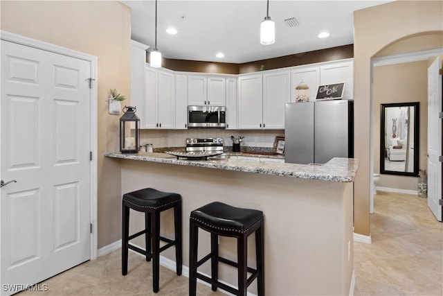 kitchen featuring light stone counters, hanging light fixtures, kitchen peninsula, stainless steel appliances, and white cabinets