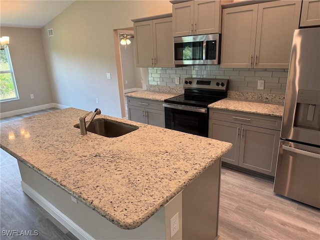 kitchen featuring sink, gray cabinets, appliances with stainless steel finishes, tasteful backsplash, and light stone countertops