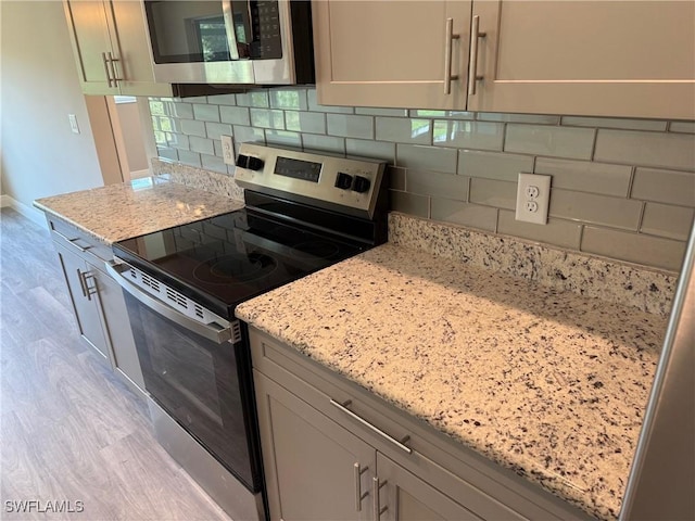 kitchen with stainless steel appliances, light wood-type flooring, backsplash, and light stone counters