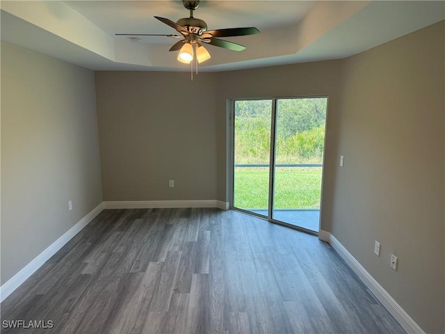 spare room featuring dark wood-type flooring, a raised ceiling, and ceiling fan