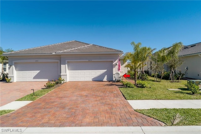 view of front facade with a tiled roof, an attached garage, decorative driveway, a front lawn, and stucco siding