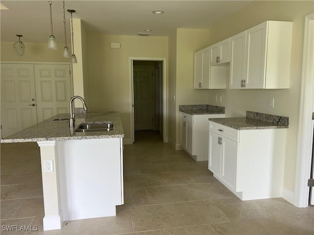 kitchen with decorative light fixtures, white cabinetry, an island with sink, sink, and light tile patterned floors