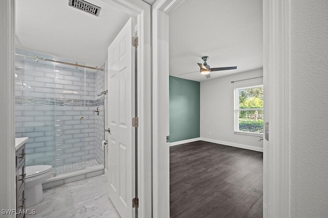 bathroom with hardwood / wood-style floors, vanity, tiled shower, ceiling fan, and toilet