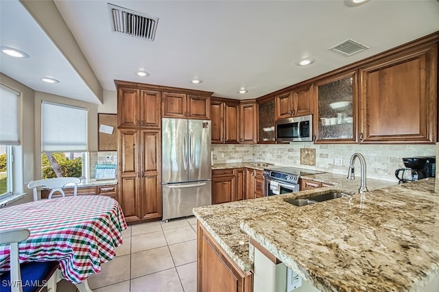 kitchen featuring sink, tasteful backsplash, light tile patterned floors, appliances with stainless steel finishes, and light stone countertops