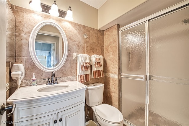 bathroom featuring vanity, toilet, a shower with shower door, and tile walls