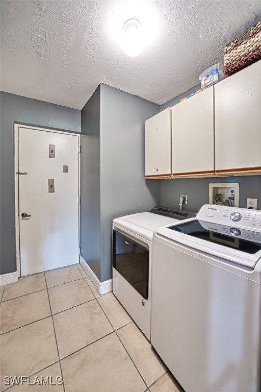 clothes washing area featuring independent washer and dryer, cabinets, a textured ceiling, and light tile patterned floors