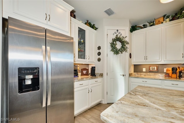 kitchen with stainless steel fridge, light stone countertops, and white cabinets