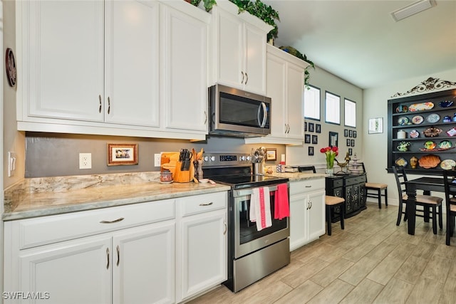 kitchen featuring light stone countertops, stainless steel appliances, white cabinets, and light wood-type flooring