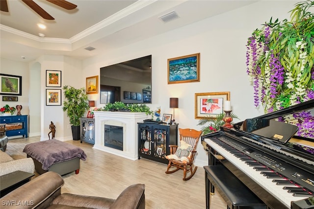 living room with a tray ceiling, ornamental molding, light hardwood / wood-style floors, and ceiling fan