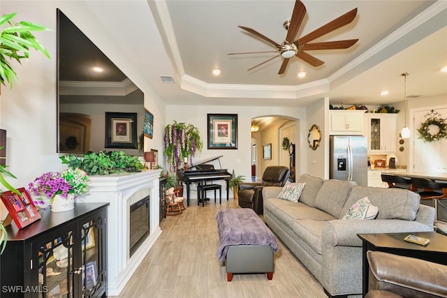 living room with crown molding, ceiling fan, a raised ceiling, and light hardwood / wood-style flooring