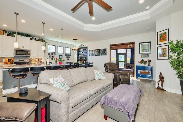 living room featuring crown molding, a tray ceiling, light hardwood / wood-style floors, and ceiling fan