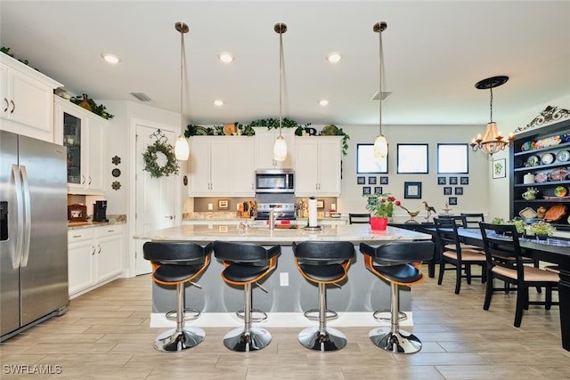 kitchen featuring pendant lighting, appliances with stainless steel finishes, an island with sink, and white cabinets