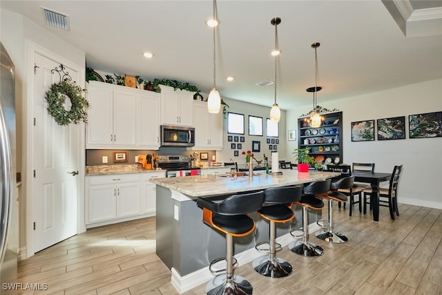 kitchen featuring white cabinetry, stainless steel appliances, decorative light fixtures, and a kitchen island with sink