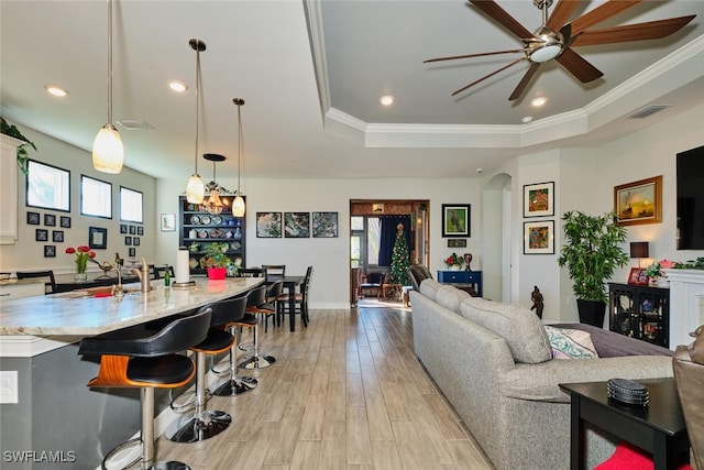 living room with a tray ceiling, ornamental molding, ceiling fan, and light wood-type flooring