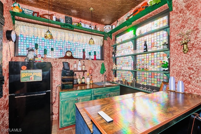 bar with black refrigerator, hanging light fixtures, sink, and wooden counters