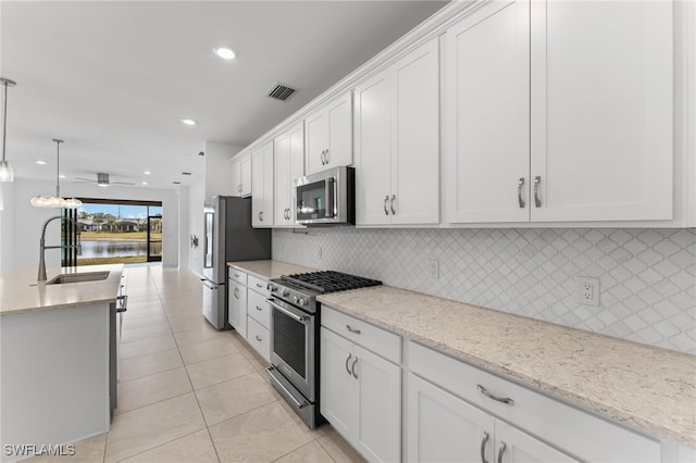 kitchen with sink, white cabinetry, light stone counters, hanging light fixtures, and appliances with stainless steel finishes