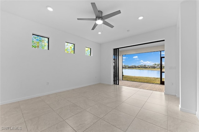 empty room with light tile patterned floors, ceiling fan, and a water view