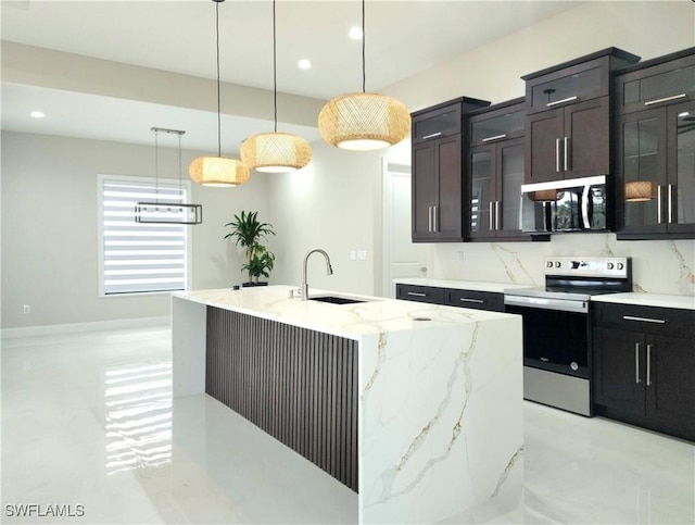 kitchen featuring appliances with stainless steel finishes, a kitchen island with sink, hanging light fixtures, light stone counters, and tasteful backsplash