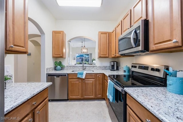 kitchen with appliances with stainless steel finishes, sink, light tile patterned floors, and light stone counters