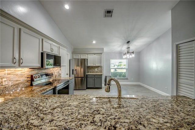 kitchen featuring appliances with stainless steel finishes, pendant lighting, lofted ceiling, backsplash, and light stone counters