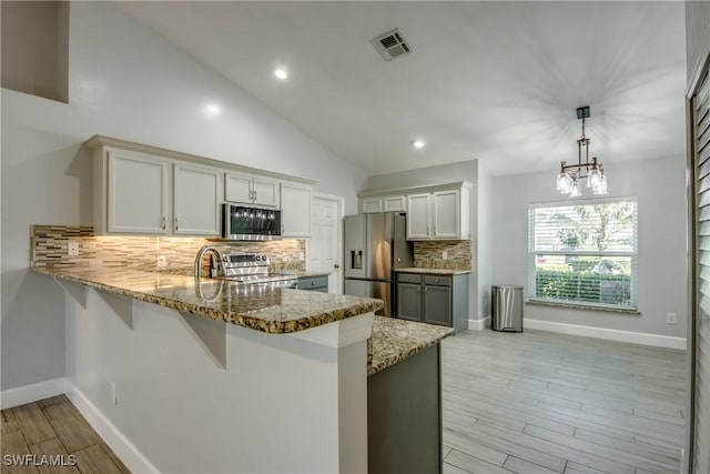 kitchen featuring pendant lighting, appliances with stainless steel finishes, vaulted ceiling, kitchen peninsula, and light wood-type flooring