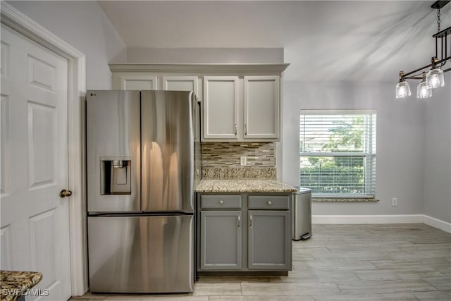 kitchen featuring gray cabinetry, stainless steel fridge with ice dispenser, pendant lighting, light stone countertops, and decorative backsplash