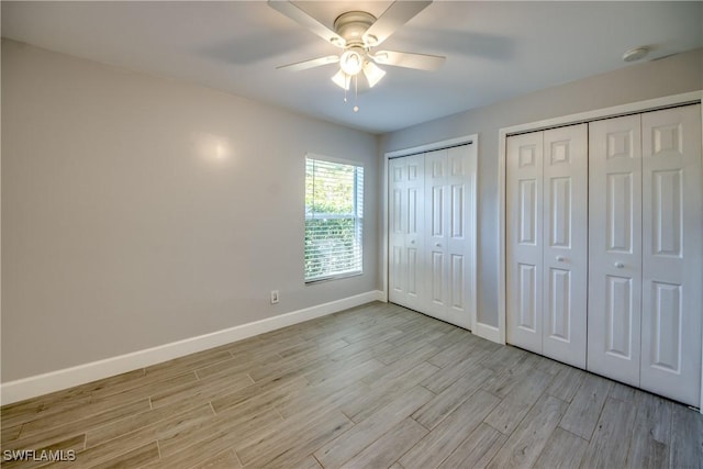 unfurnished bedroom featuring ceiling fan, multiple closets, and light wood-type flooring