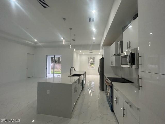 kitchen featuring appliances with stainless steel finishes, white cabinetry, sink, hanging light fixtures, and a center island with sink