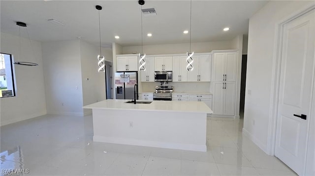 kitchen featuring a kitchen island with sink, stainless steel appliances, a sink, baseboards, and white cabinets