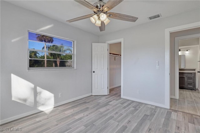 unfurnished bedroom with a walk in closet, light hardwood / wood-style flooring, a closet, and ceiling fan