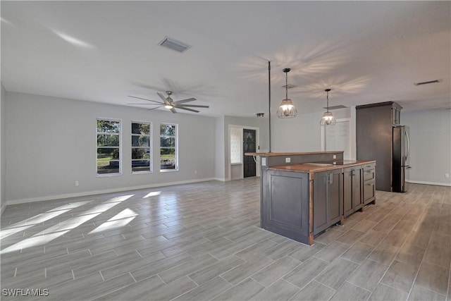 kitchen with stainless steel fridge, hanging light fixtures, a center island, dark brown cabinetry, and ceiling fan with notable chandelier