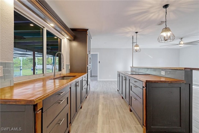 kitchen featuring butcher block counters, sink, dark brown cabinets, and hanging light fixtures