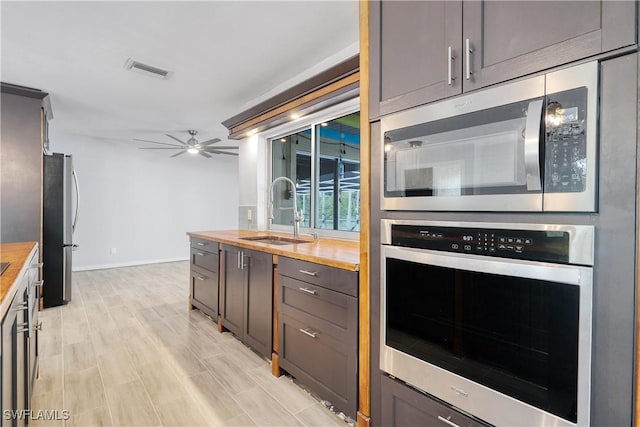 kitchen with sink, butcher block countertops, light wood-type flooring, ceiling fan, and stainless steel appliances