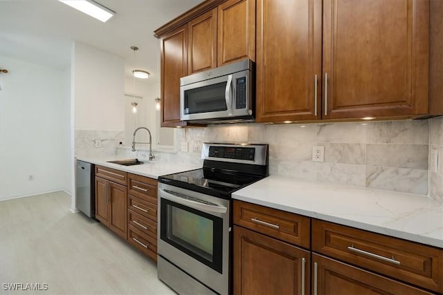 kitchen with sink, light stone counters, light wood-type flooring, appliances with stainless steel finishes, and backsplash