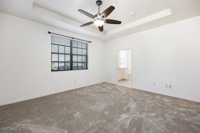 unfurnished room featuring light carpet, a tray ceiling, a ceiling fan, and baseboards