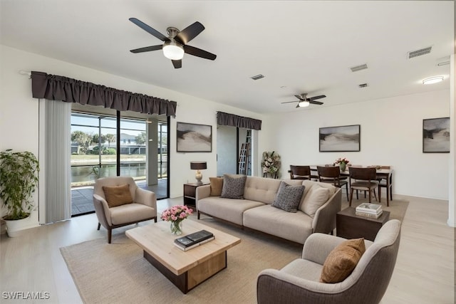 living area with light wood-style flooring, visible vents, and ceiling fan