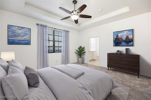 bedroom featuring ceiling fan, ensuite bath, a raised ceiling, and light colored carpet