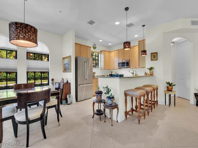 kitchen featuring stainless steel appliances, light brown cabinetry, kitchen peninsula, and hanging light fixtures