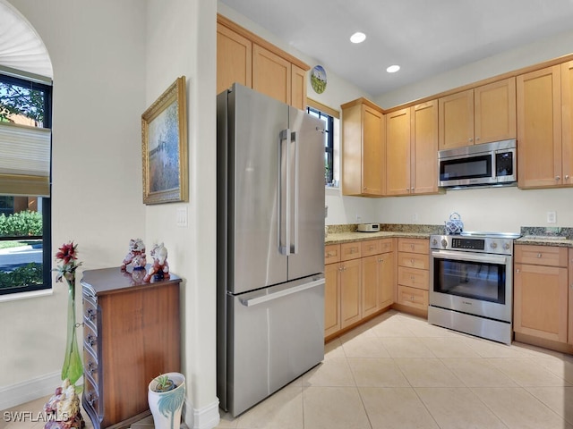 kitchen with stainless steel appliances, light stone countertops, and light brown cabinets