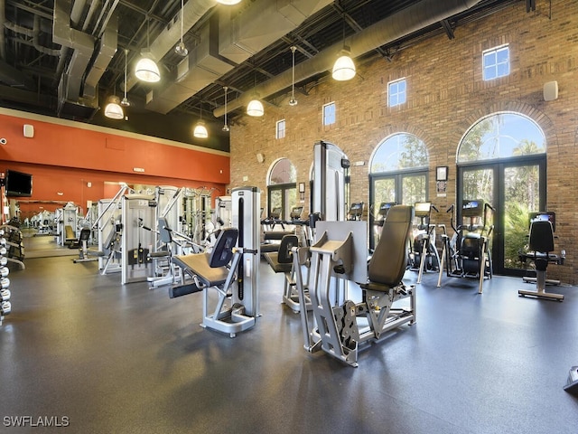 exercise room with french doors, a high ceiling, and brick wall